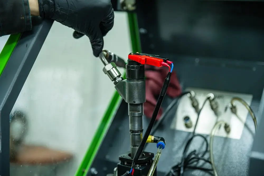 Technician in black gloves inspecting a fuel injection component